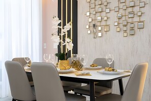 A modern dining area with a white table set for four, surrounded by grey chairs. A decorative wall with geometric patterns and a vertical gold strip is visible behind the table. - Disney 4BR Home w/ Pool + Themed Bedrooms (Kissimmee)