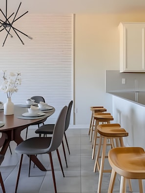 A modern dining area with a long table, several chairs, and a kitchen area with cabinets. - 3BR Villa w/ Resort Access Near Disney (Davenport)