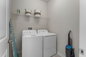 A laundry room with two white washing machines, a shelf with bottles, and a vacuum cleaner. - 3BR Villa w/ Resort Access Near Disney (Davenport)