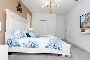 Een slaapkamer met een groot bed, een kroonluchter, een televisie aan de muur en een deur op de achtergrond.