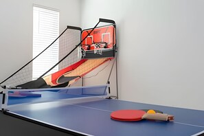 A ping pong table with a red paddle and a ball, a window with blinds, and a red exercise machine. - 9BR Villa w/ Pool & Game Room Near Disney (Davenport)