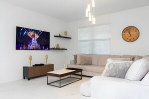 A modern living room with a flat-screen TV, a coffee table, a sofa, and a clock on the wall. - 9BR Villa w/ Pool & Game Room Near Disney (Davenport)