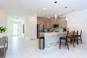 Een moderne keuken met een marmeren eiland, roestvrijstalen apparatuur en houten stoelen.