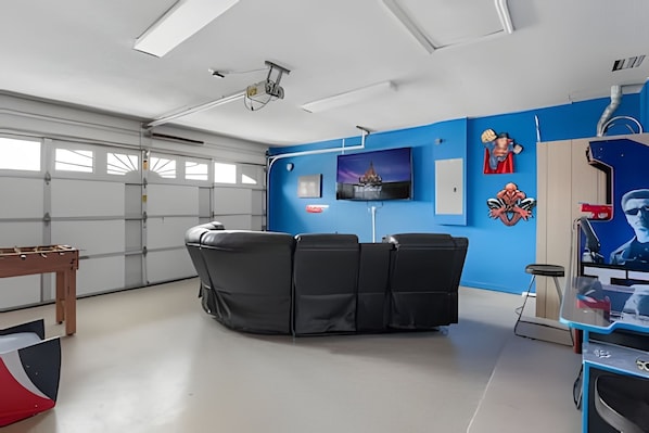 A room with a blue wall, a mounted TV, and a ceiling projector. - 4BR Pool Home Near Disney + Game Room (Kissimmee)