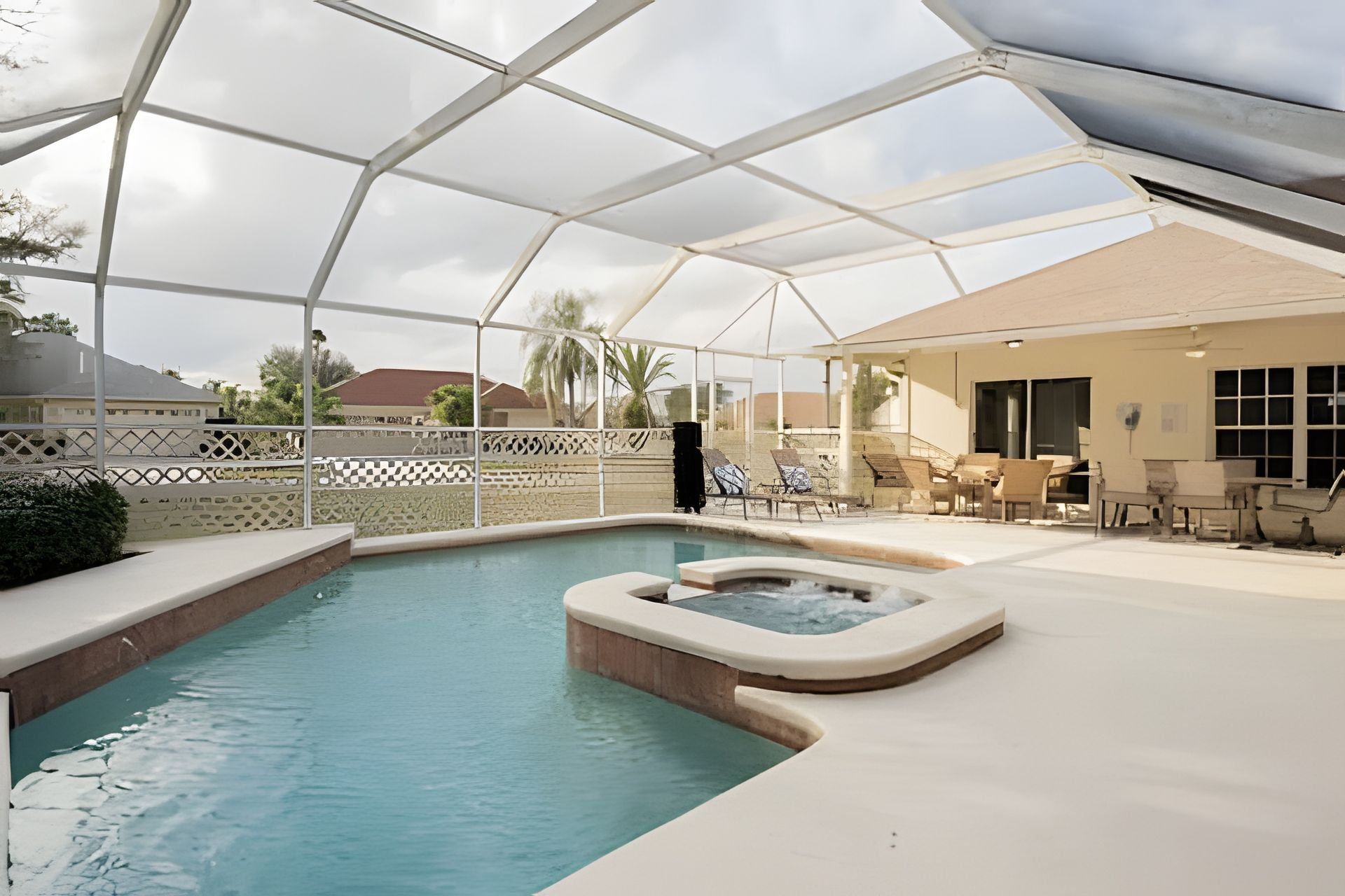 A pool area with a hot tub, lounge chairs, and a covered patio.