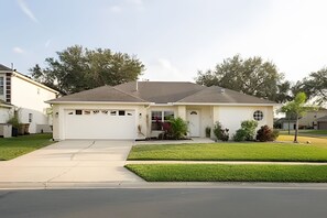 A single-story house with a garage, a front yard with grass and a small tree, and a driveway leading to the garage. - 4BR Pool Home Near Disney + Game Room (Kissimmee)