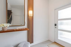A hallway with a white door, a wooden bench, a mirror, and a wall-mounted light fixture. - Storey Lake 4BR w/ Pool + Disney-themed Rooms (Kissimmee)