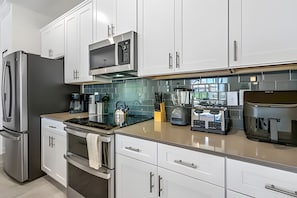 A modern kitchen with stainless steel appliances, white cabinetry, and a large island with a built-in coffee maker. - Storey Lake 4BR w/ Pool + Disney-themed Rooms (Kissimmee)