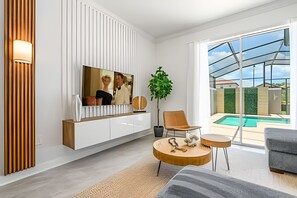 A modern living room with a large TV, a plant, a pool, and a grey sofa. - Storey Lake 4BR w/ Pool + Disney-themed Rooms (Kissimmee)