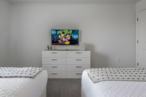 A bedroom with a TV on the wall, a white dresser, two beds with patterned bedding, and a carpeted floor. - Storey Lake 4BR w/ Pool + Disney-themed Rooms (Kissimmee)