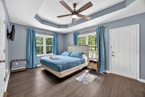 A bedroom with a bed, a ceiling fan, a nightstand, a window with curtains, and a door. - Lovely Truist Retreat | Cozy 4 Bed with Fire Pit (Marietta)