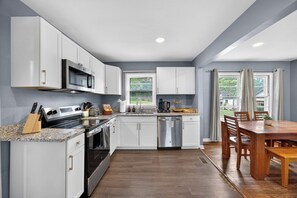 A modern kitchen with white cabinets, a stainless steel microwave, and a dishwasher. - Lovely Truist Retreat | Cozy 4 Bed with Fire Pit (Marietta)
