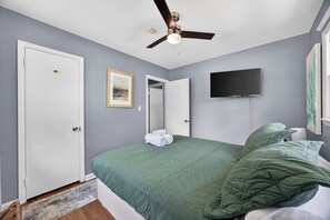 Un dormitorio con una cama, ventilador de techo, televisión de pantalla plana y una puerta.