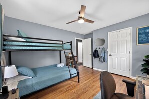 A room with a bunk bed, a desk with a chair, a ceiling fan, and a door. - Lovely Truist Retreat | Cozy 4 Bed with Fire Pit (Marietta)