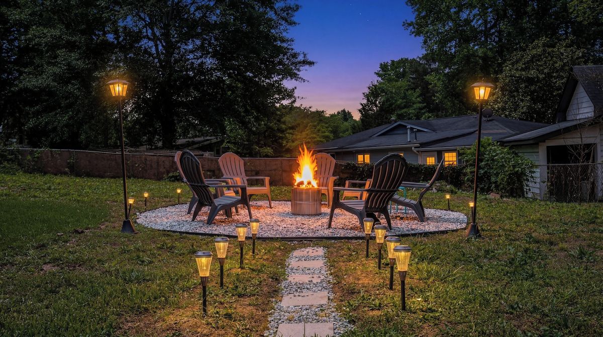 An outdoor seating area with a fire pit, surrounded by chairs and illuminated by lanterns.