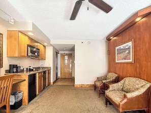 A compact living space with a kitchenette, a ceiling fan, a framed picture on the wall, and a carpeted floor. - NEW - Stellar Location with Hot Tub, Pool, Steam Room & Gym Acces, Pets Okay (Crested Butte)