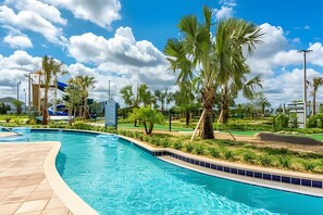 A swimming pool with a tiled deck, surrounded by palm trees and greenery, with a clear sky above. - Charming 4BR w/ Pool Near Disney - Storey Lake (Kissimmee)