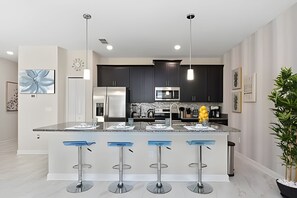 A modern kitchen with dark cabinets, stainless steel appliances, and a central island with bar stools. - Charming 4BR w/ Pool Near Disney - Storey Lake (Kissimmee)