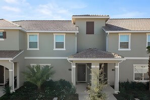 A row of two-story townhouses with a tiled roof, a central entrance, and a small garden area. - Charming 4BR w/ Pool Near Disney - Storey Lake (Kissimmee)