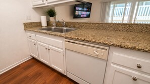 A kitchen with a granite countertop, stainless steel sink, white cabinets, and a dishwasher. - Ocean Escape | Beach Front Getaway, Steps to Sand (Redondo Beach)