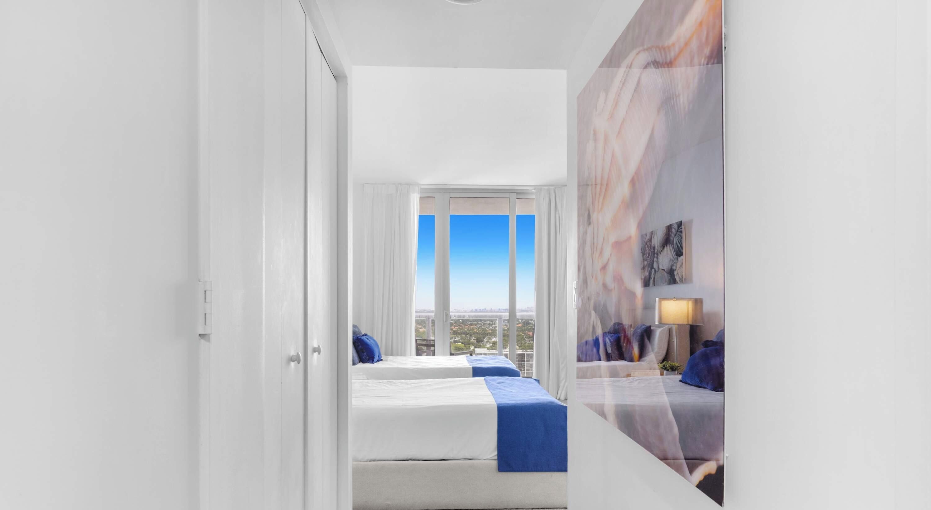 Habitación de hotel con un ventanal grande, una cama, un escritorio y vistas a la ciudad.