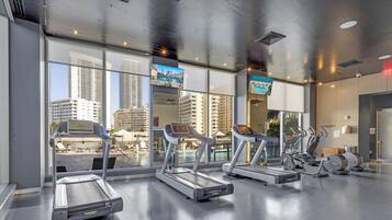 Un gimnasio con cintas de correr, bicicletas estáticas y vista a la piscina.