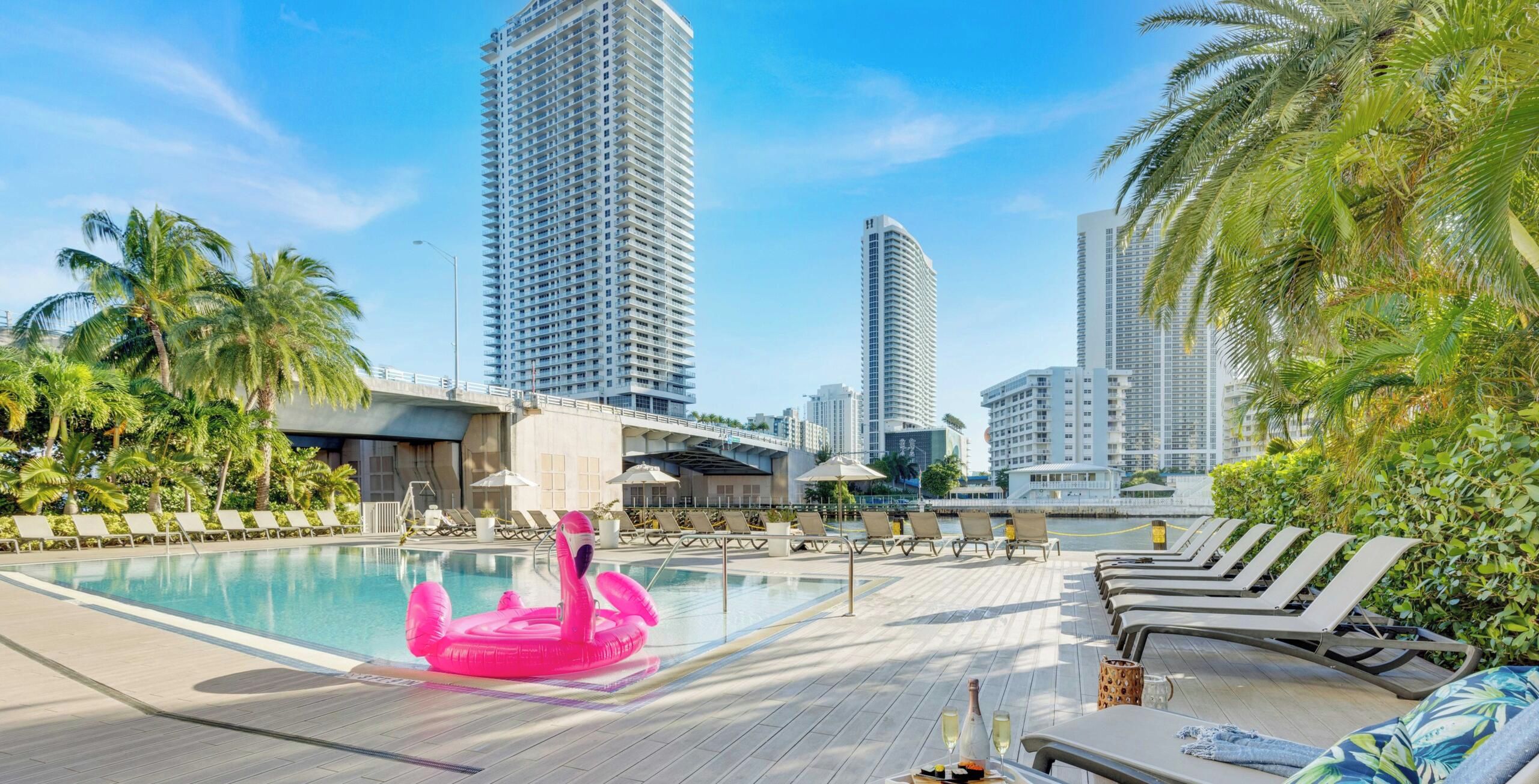 A pool area with lounge chairs, a decorative flamingo float, and high-rise buildings in the background.