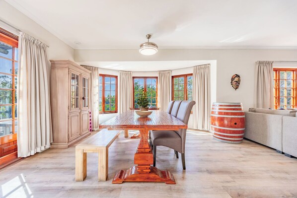 A dining area with a wooden table, chairs, a bench, and a large window with curtains.
