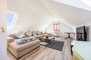 A spacious loft apartment with a high ceiling, a large sofa set, a dining table, and a television.