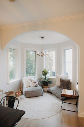 A cozy room with a curved ceiling, a chandelier, a large window, a seating area with cushions, a plant, and a small table. - Nordic Spa Lakefront Retreat | Sauna + Lake Plunge (Leeds and the Thousand Islands)