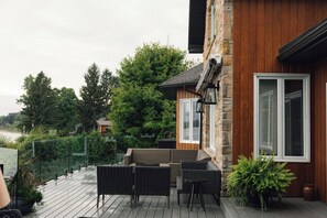 A wooden deck with wicker furniture, a stone wall, and a view of a lake.