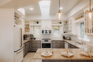 A modern kitchen with white cabinetry, a central island with a dining setup, and a skylight. - Nordic Spa Lakefront Retreat | Sauna + Lake Plunge (Leeds and the Thousand Islands)