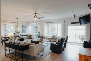 A spacious living room with a ceiling fan, a dining area with a table and chairs, and a large window offering a view. - Nordic Spa Lakefront Retreat | Sauna + Lake Plunge (Leeds and the Thousand Islands)