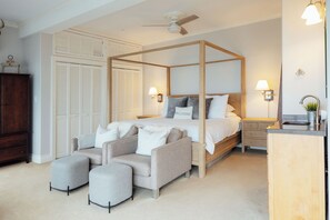 Ein Schlafzimmer mit einem Himmelbett, einem Nachttisch aus Holz, einer Kommode und einer Sitzecke mit zwei Sesseln.