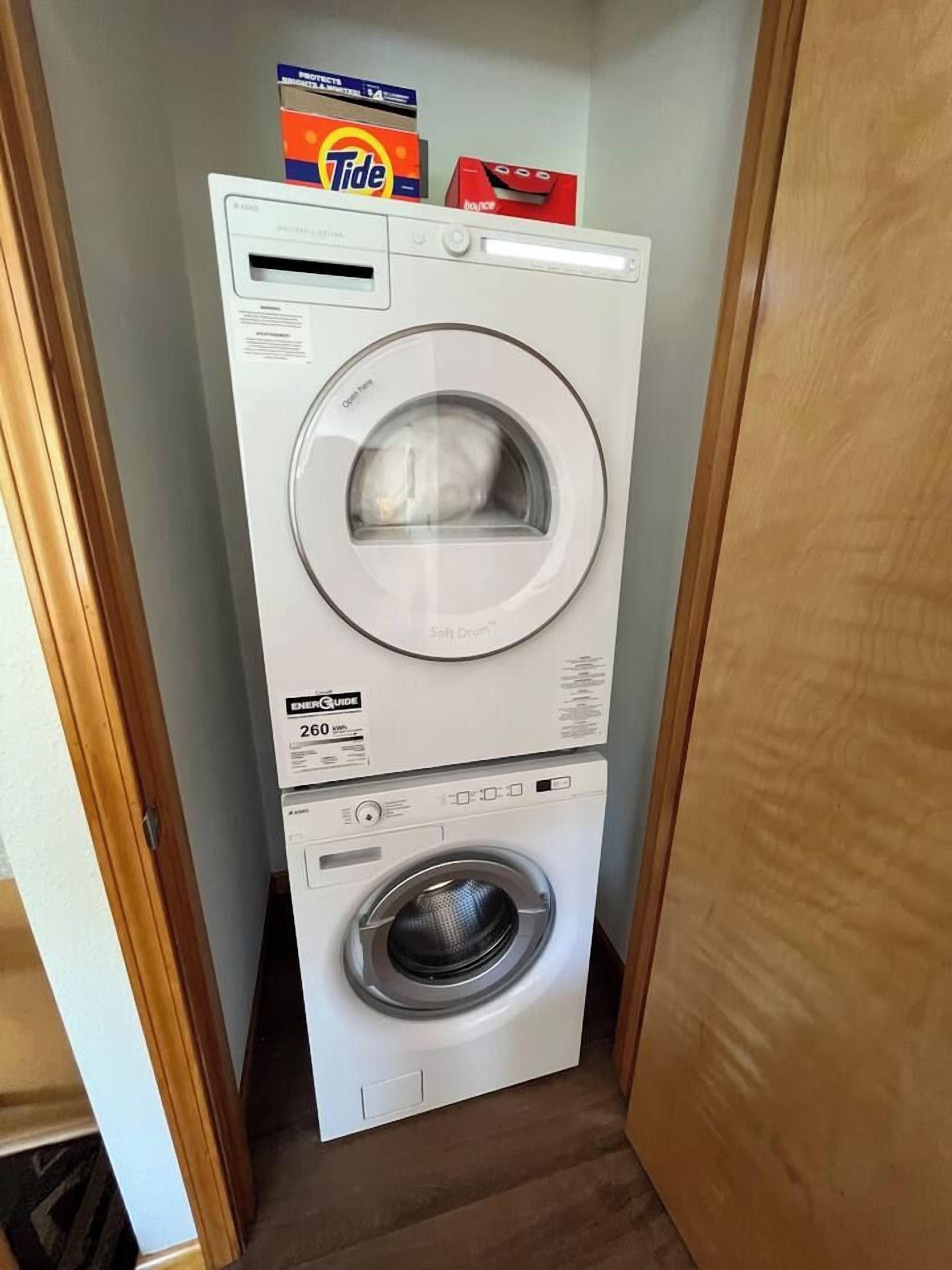Un appareil compact combinant lave-linge et sèche-linge, conçu pour les petits espaces, avec un compartiment pour la lessive Tide placé sur le dessus.
