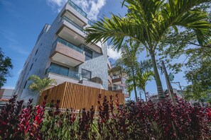 A multi-story building with balconies, a wooden fence, and tropical plants. - IBIZA Ap. 209 Balta (Ipojuca)