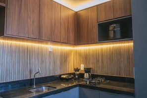 A modern kitchen with wooden cabinets, a stainless steel sink, and a coffee maker. - IBIZA Ap. 209 Balta (Ipojuca)