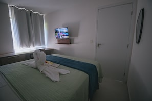 A hotel room with a bed, a television on a stand, a door, and a window with curtains. - IBIZA Ap. 209 Balta (Ipojuca)