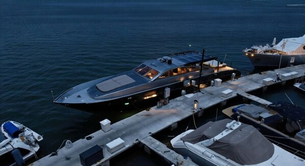 A large yacht docked at a marina with a covered deck area and multiple smaller boats nearby.