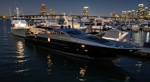 A marina with multiple yachts docked, a bridge in the background, and a city skyline.