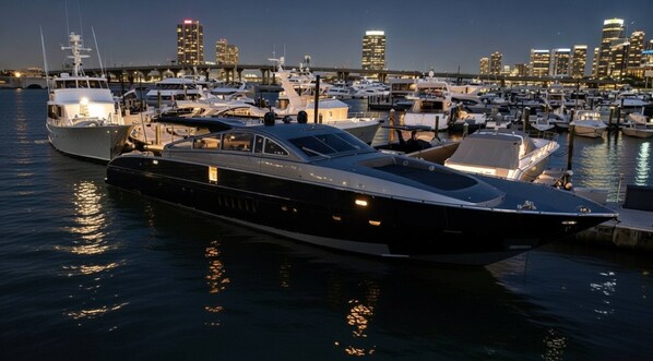 A marina with multiple yachts docked, a bridge in the background, and a city skyline.