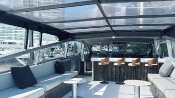 Un intérieur de bateau moderne avec un bar, des sièges et de grandes fenêtres offrant une vue sur la ville.