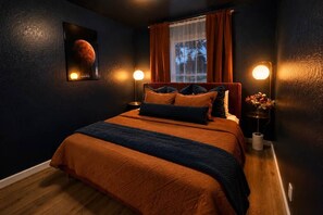 A bedroom with a large bed, a window with curtains, a wall-mounted lamp, and a poster of Mars. - Space City | Work Stays • Family Fun • 3BR (Weatherford)