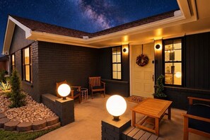 A house exterior at night with a starry sky, a porch with seating, and a wreath on the door. - Space City | Work Stays • Family Fun • 3BR (Weatherford)