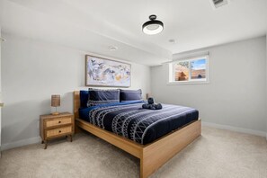 Un dormitorio con cama, mesita de noche, lámpara de pared y ventana con vistas.