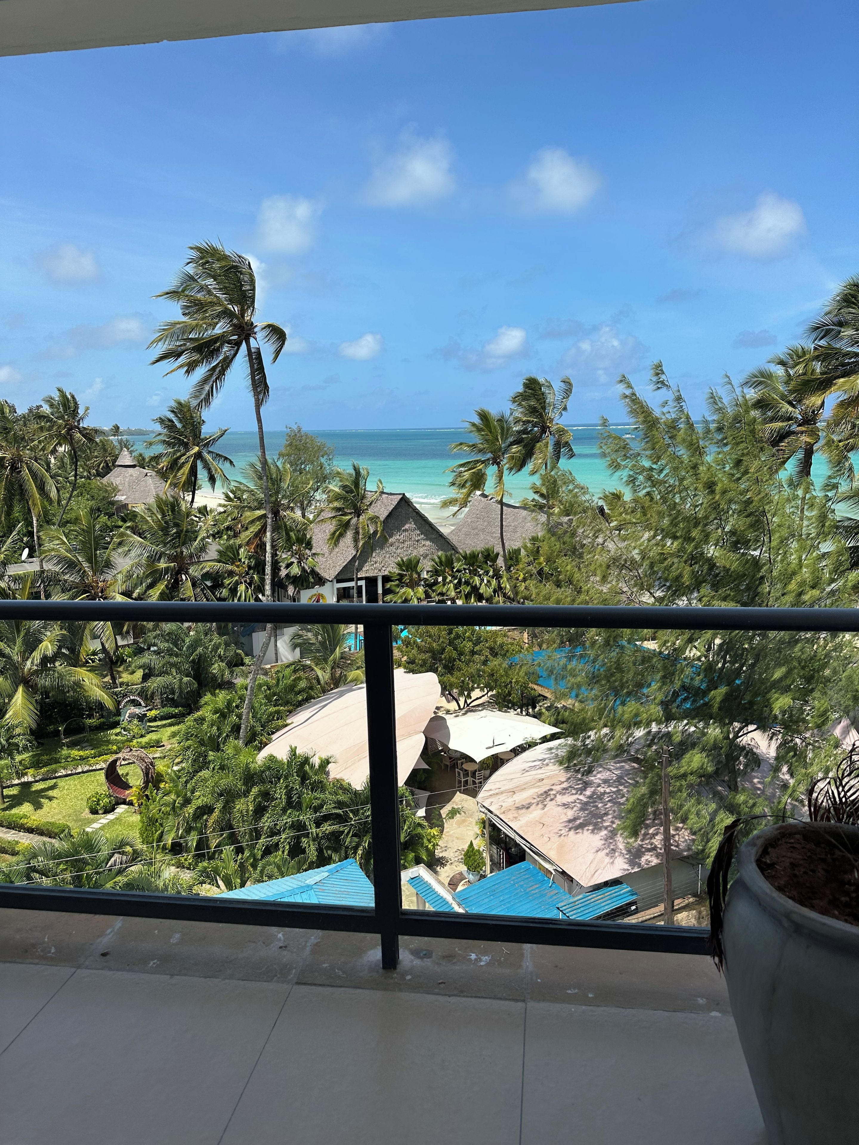 Un balcón con vista a una playa, palmeras y una zona turística.