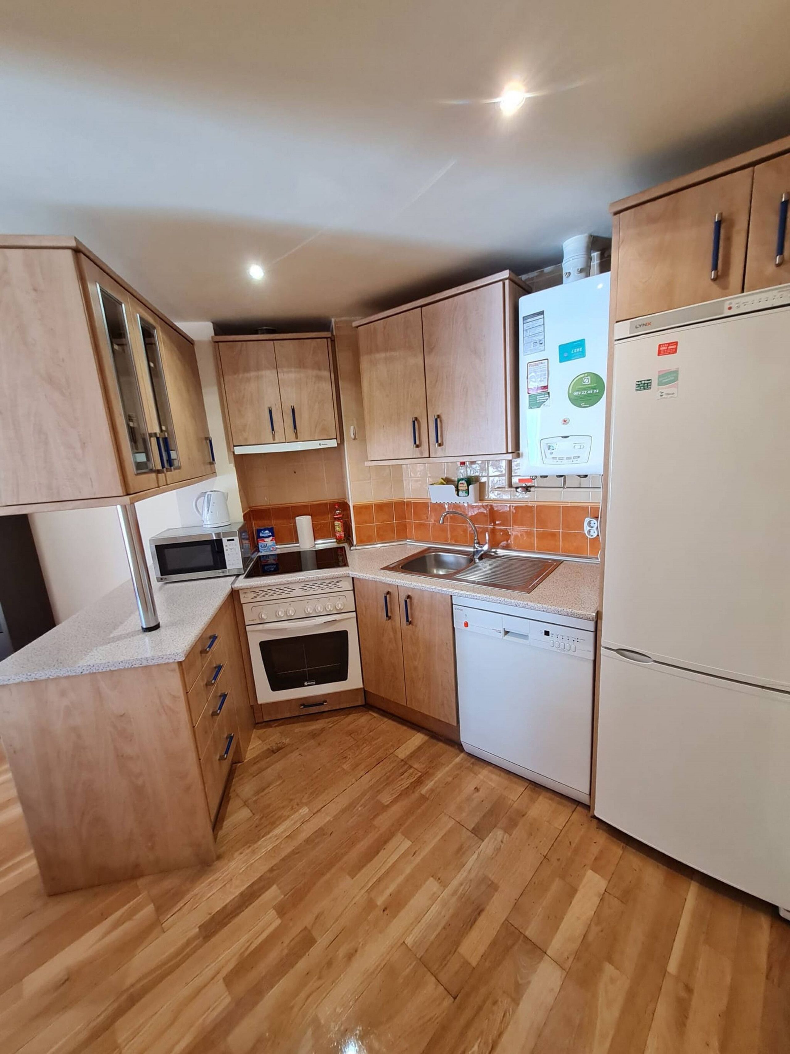 Cocina compacta con armarios de madera, microondas, horno, lavavajillas y refrigerador.