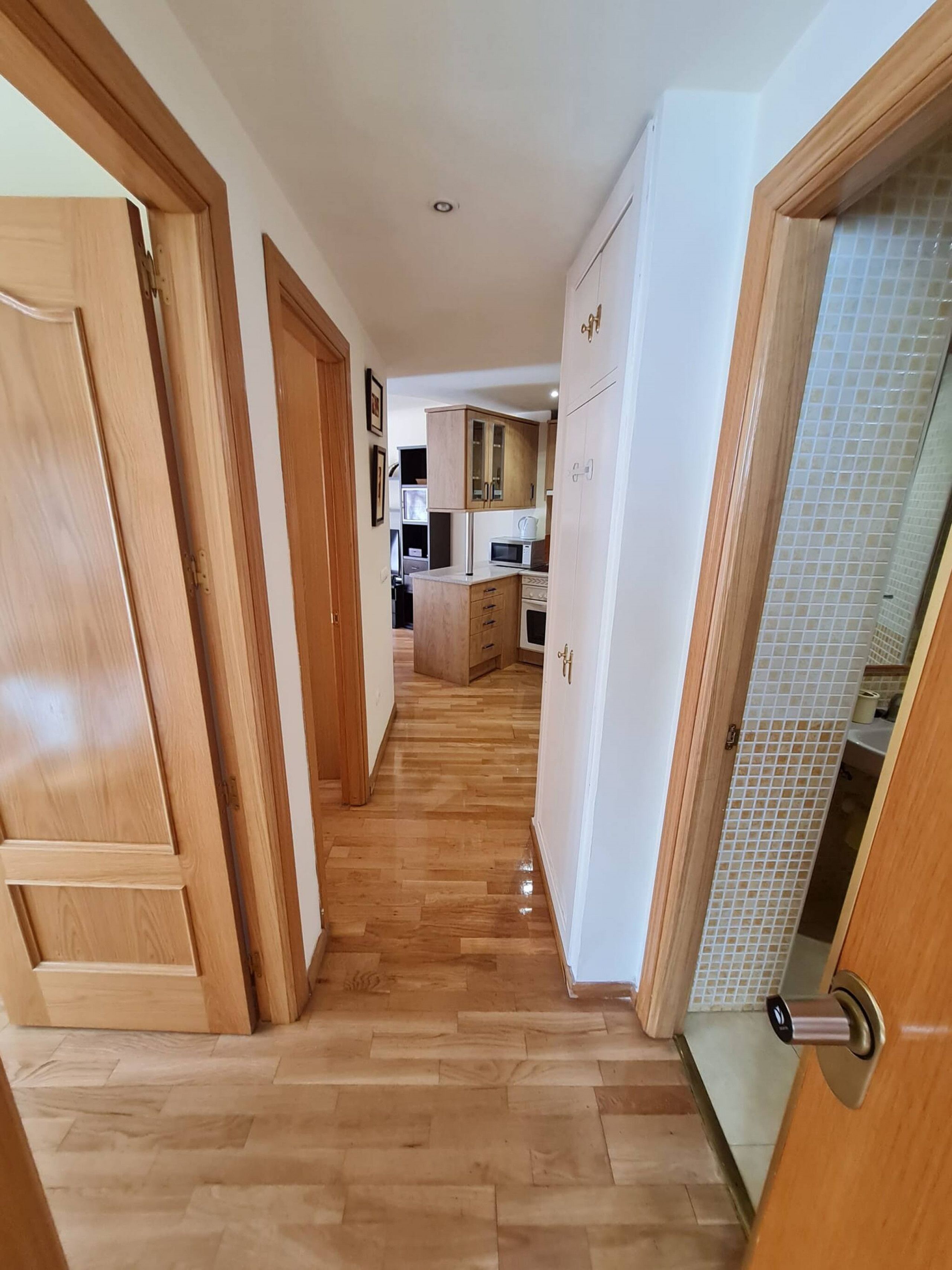 Un pasillo con suelo de madera que conduce a una cocina con armarios y electrodomésticos.