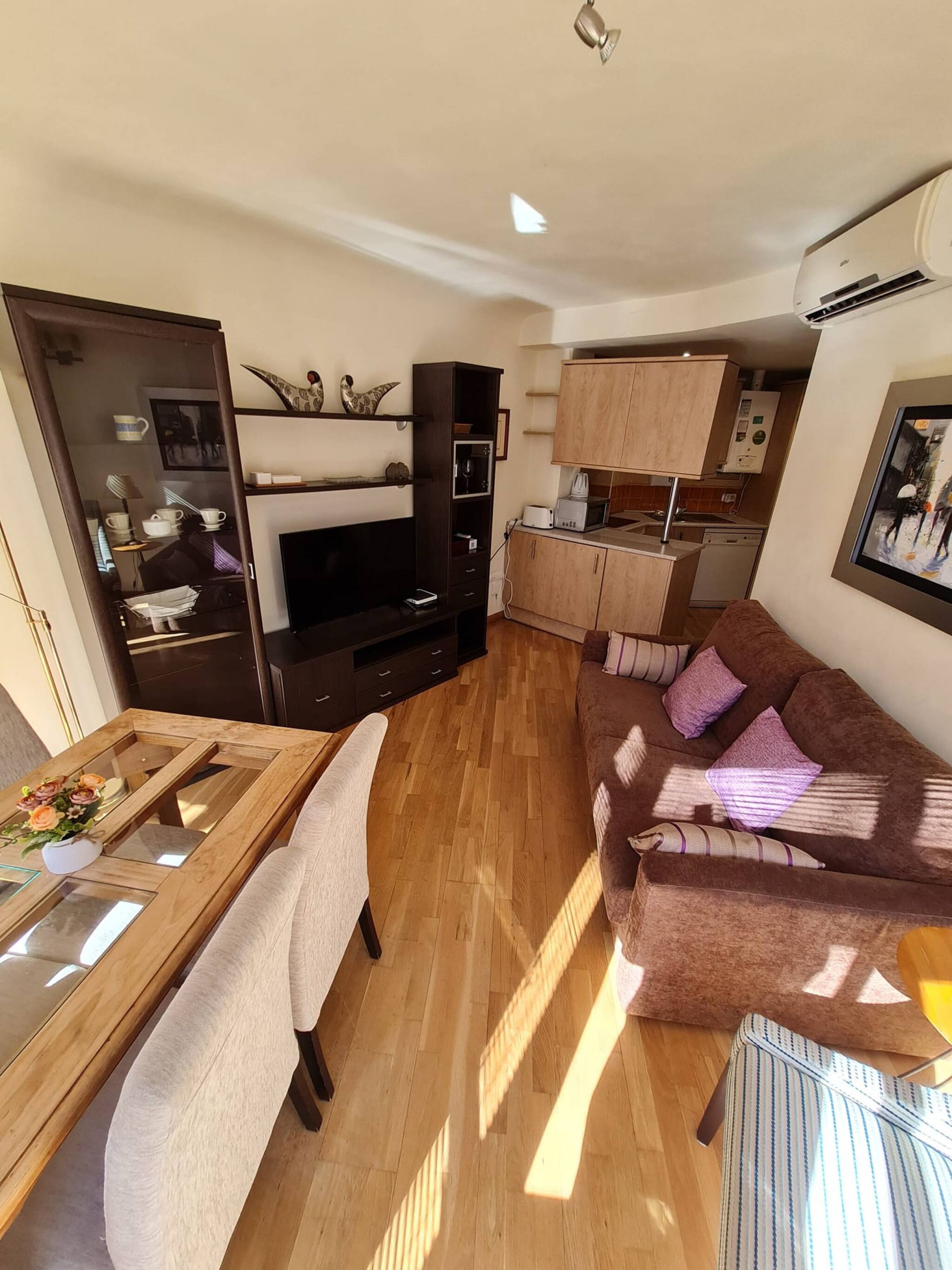 Un espacio habitable compacto con sofá, una mesa de comedor, televisor y kitchenette.