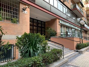 Un edificio residencial de varios pisos con fachada de ladrillo, una entrada visible con un portón negro y una escalera que conduce a la entrada.